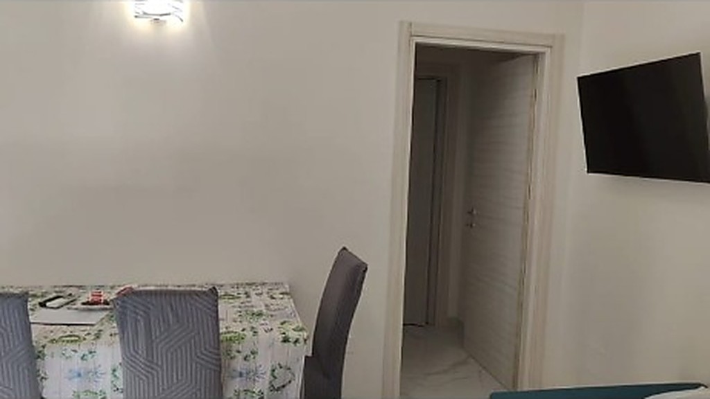 Zona pranzo con tavolo, sedute imbottite e Smart TV a parete